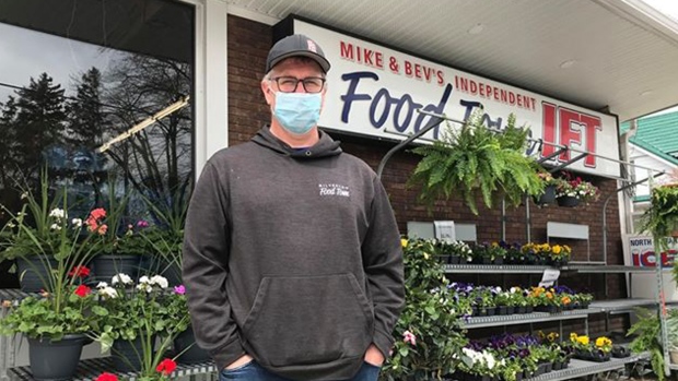 A man with a masks stands outside a grocery store